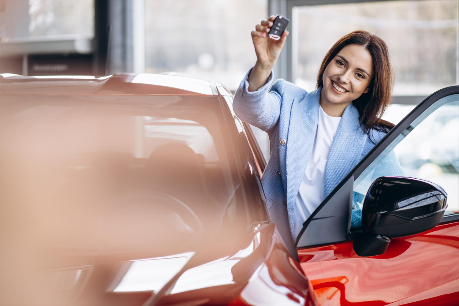 Žena podiže ključ pored automobila pri preuzimanju vozila